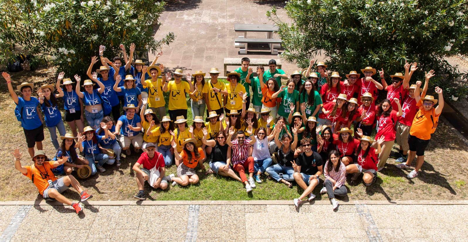 foto com dezenas de jovens com t-shirts de várias cores em pé e sentados num jardim de baços no ar
