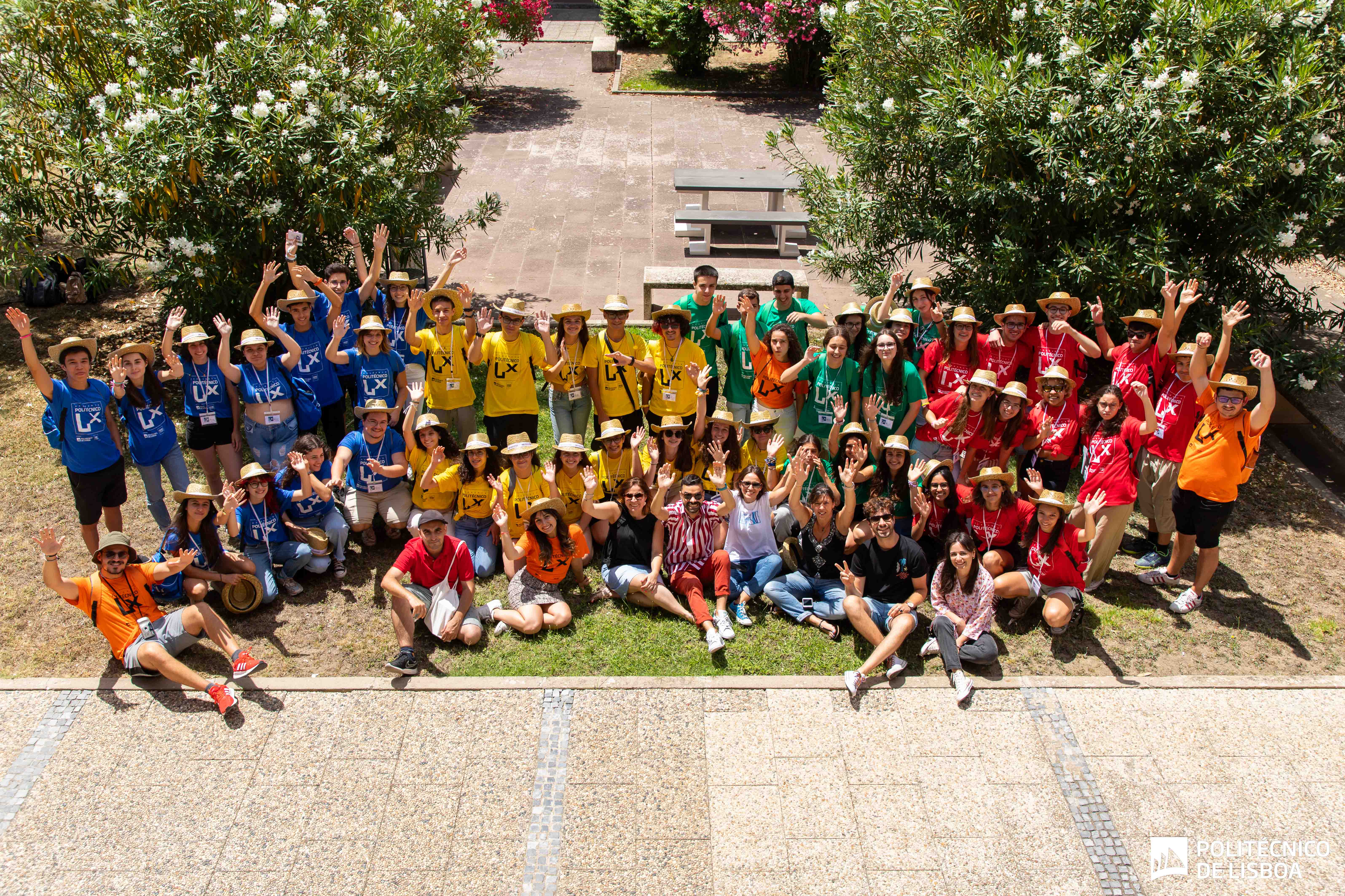 foto com dezenas de jovens com t-shirts de várias cores em pé e sentados num jardim de baços no ar
