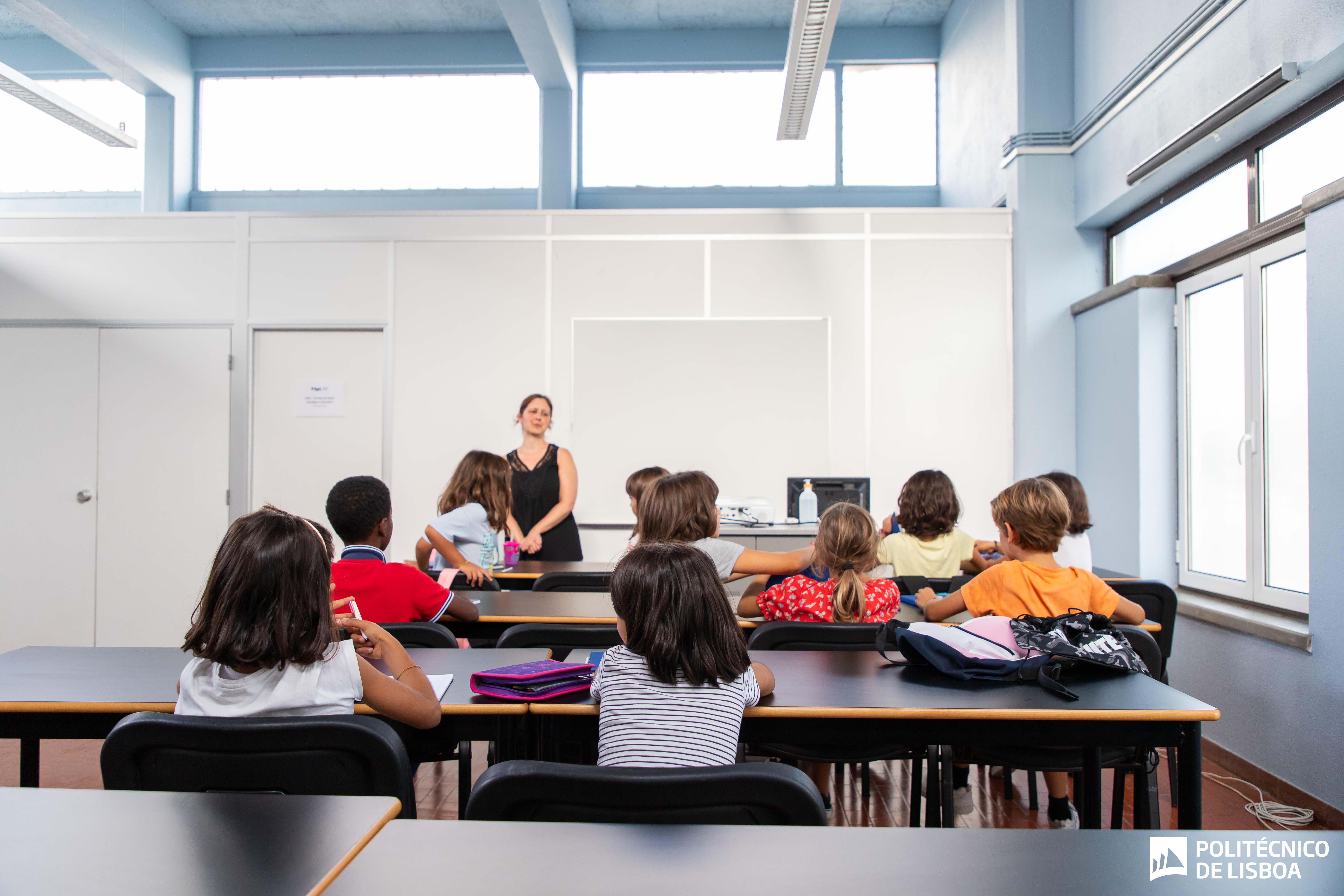 crianças sentadas numa sala de aula viradas para a professora