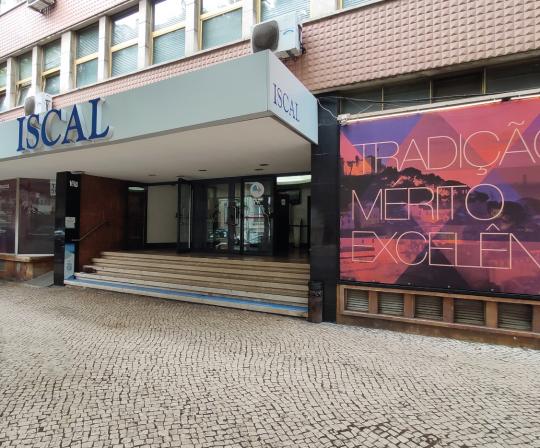 Imagem da entrada do prédio do ISCAL, onde se vê as escadas e à direita uma lona em tons quentes