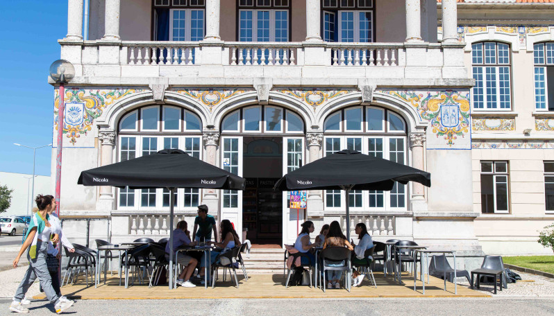 esplanada de bar com chapéus e pessoas sentadas nas mesas e pessoas a passar a pé