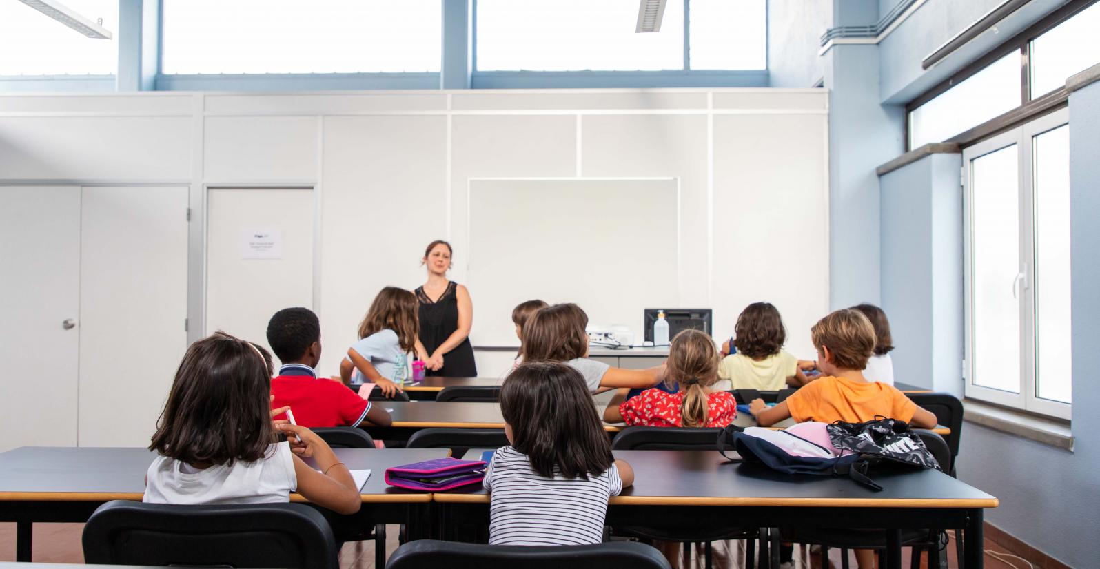 crianças sentadas numa sala de aula viradas para a professora