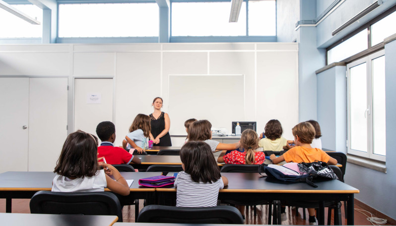 crianças sentadas numa sala de aula viradas para a professora