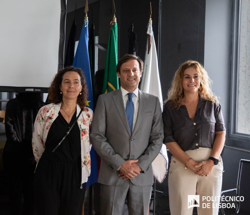 foto com duas mulheres e um homem ao centro, em pé frente a bandeiras