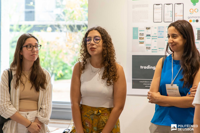 foto de 3 mulheres de pé junto a paineis expostos na parede