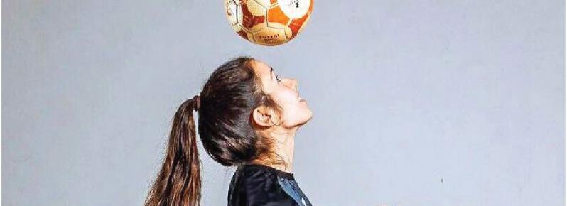 uma rapariga equipada a dar toques numa bola com a cabeça