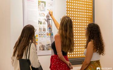 foto de 3 raparigas de pé a observar um painel pendurado na parede com trabalhos de designs 