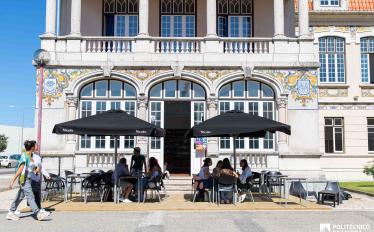 esplanada de bar com chapéus e pessoas sentadas nas mesas e pessoas a passar a pé