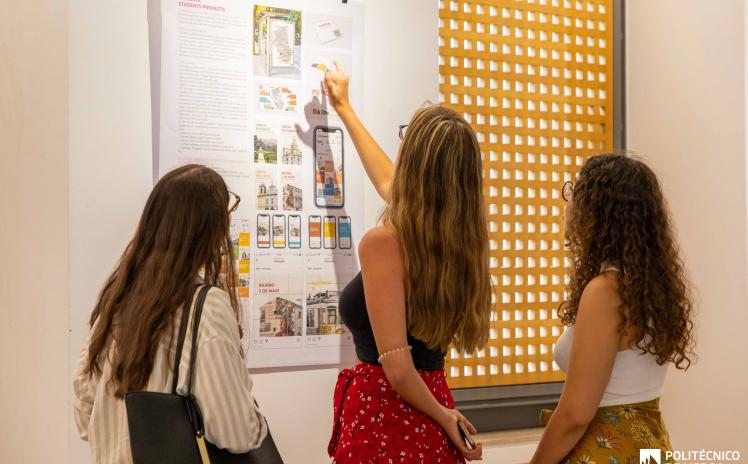 foto de 3 raparigas de pé a observar um painel pendurado na parede com trabalhos de designs 