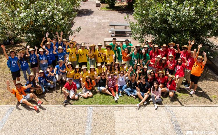 foto com dezenas de jovens com t-shirts de várias cores em pé e sentados num jardim de baços no ar