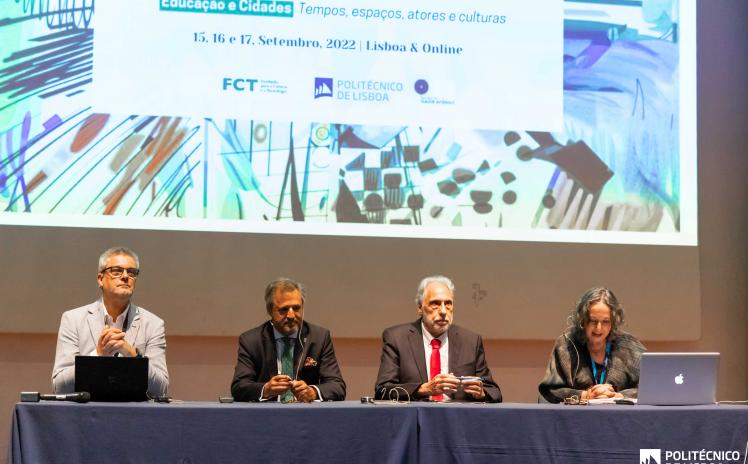 3 homens e 1 mulher sentados numa mesa num palco com uma projeção