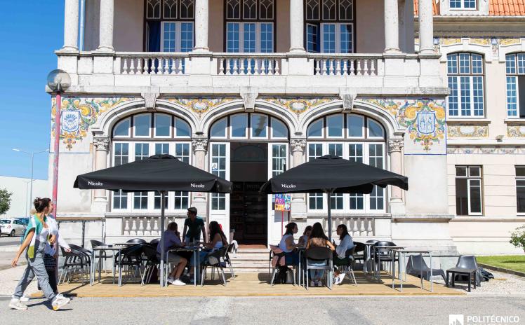 esplanada de bar com chapéus e pessoas sentadas nas mesas e pessoas a passar a pé