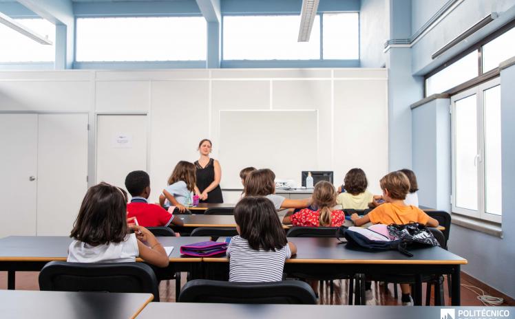 crianças sentadas numa sala de aula viradas para a professora